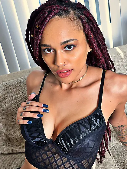 Black chick with long legs and pierced nostril poses on sofa wit