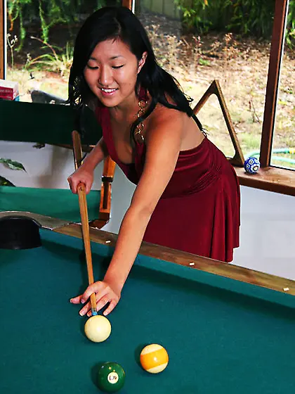 Asian babe in maroon dress climbs the pool table to pose without
